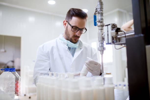 Close up of focused serious fabric worker with taken off face mask holding a bottle of liquid soap with a row in front.